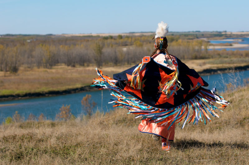 woman First Nations fancy shawl dance in a field alongside the river 