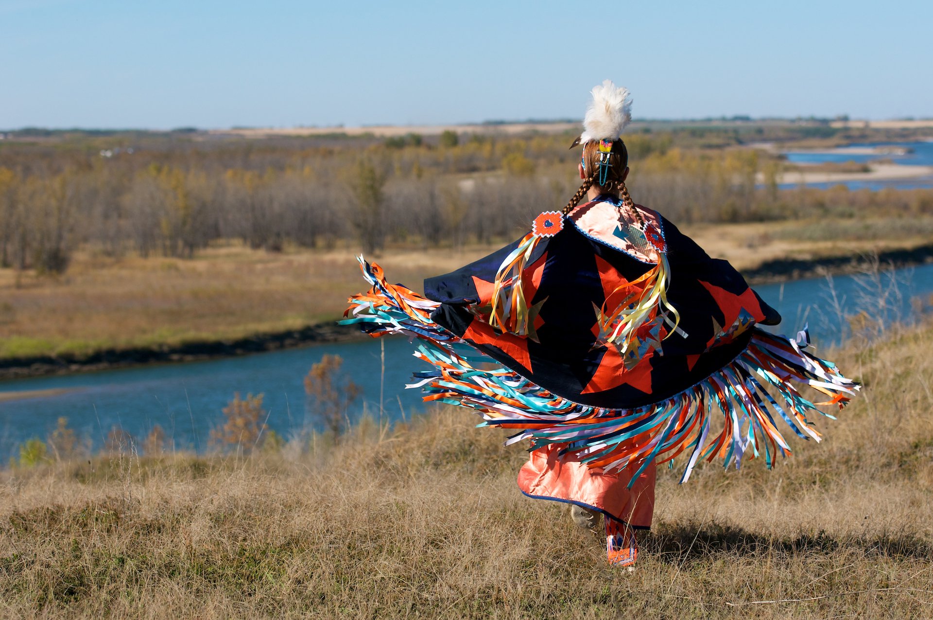 woman First Nations fancy shawl dance in a field alongside the river